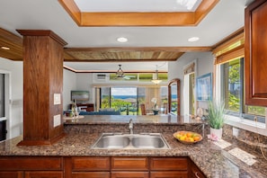 A kitchen with granite countertops, wooden cabinets, a double sink, and a view of the outdoors. - Two-Story Ocean View Retreat Steps from Pool & Beaches -KRV 915 (Lahaina)