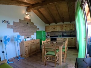 A rustic kitchen with wooden cabinets, a green refrigerator, and a dining area with wooden chairs and a table. - On Kiniperu (Tasonis)