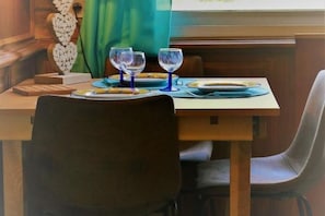 Ein Esstisch ist gedeckt mit Tellern, Besteck und Weingläsern, im Hintergrund steht ein Stuhl und ein dekoratives Wandbild.