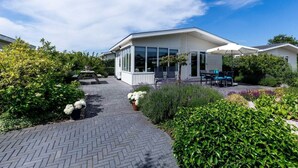 Una casa moderna con un porche cubierto, un camino de entrada pavimentado y abundante vegetación.