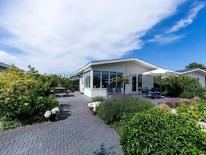 A modern house with a covered patio, a paved driveway, and lush greenery. - Holiday Home in Noordwijk With Terrace (Noordwijk)
