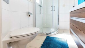 Un baño moderno con inodoro, cabina de ducha de vidrio y tocador de madera.