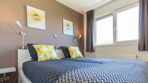 Un dormitorio con una cama, dos lámparas de pared y dos cuadros colgados.