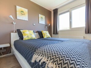 A bedroom with a bed, two wall-mounted lamps, and two wall-mounted paintings. - Holiday Home in Noordwijk With Terrace (Noordwijk)