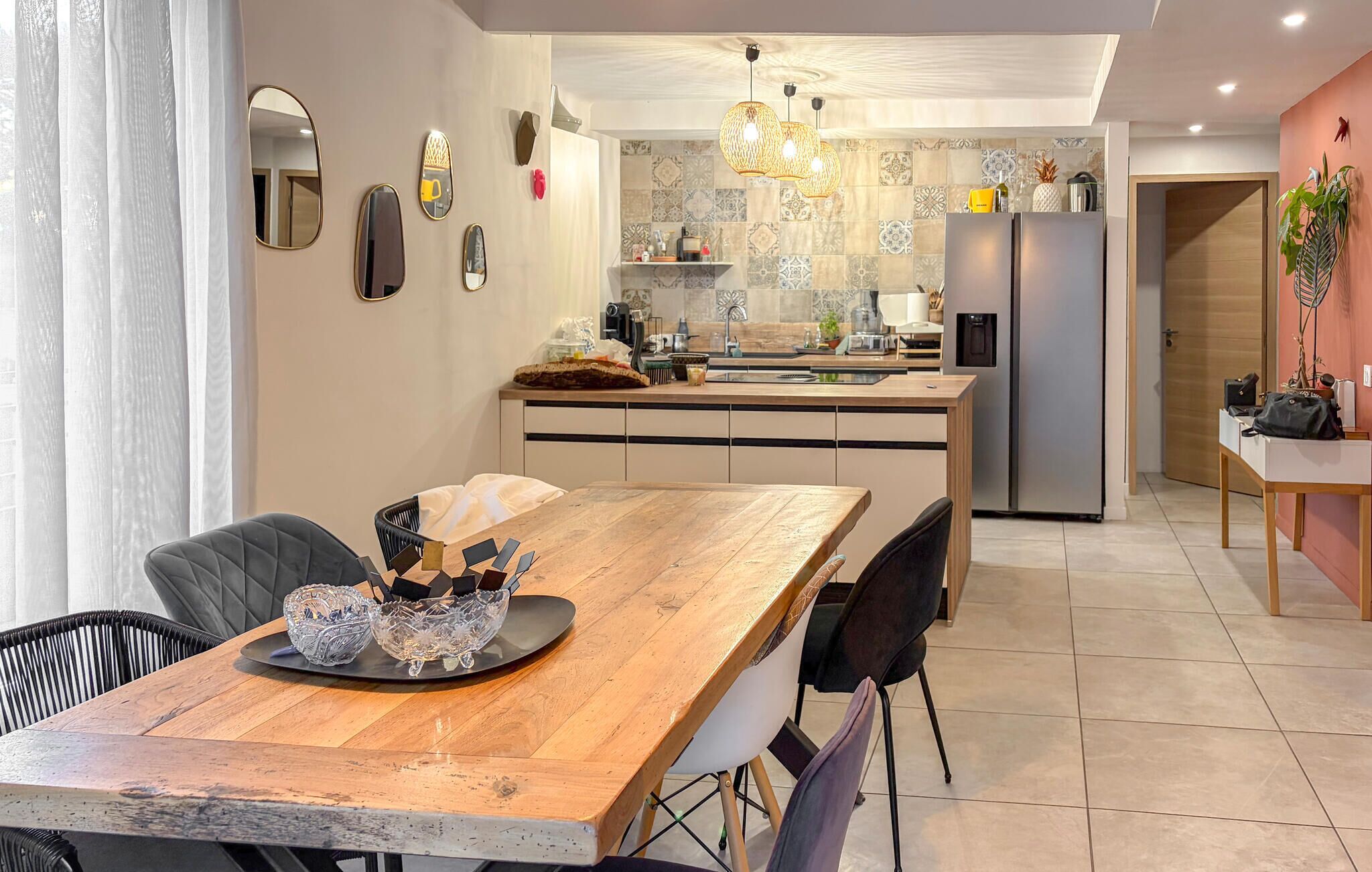 Une cuisine moderne dotée d’un îlot central, de luminaires suspendus et d’un coin repas avec une table et des chaises en bois.