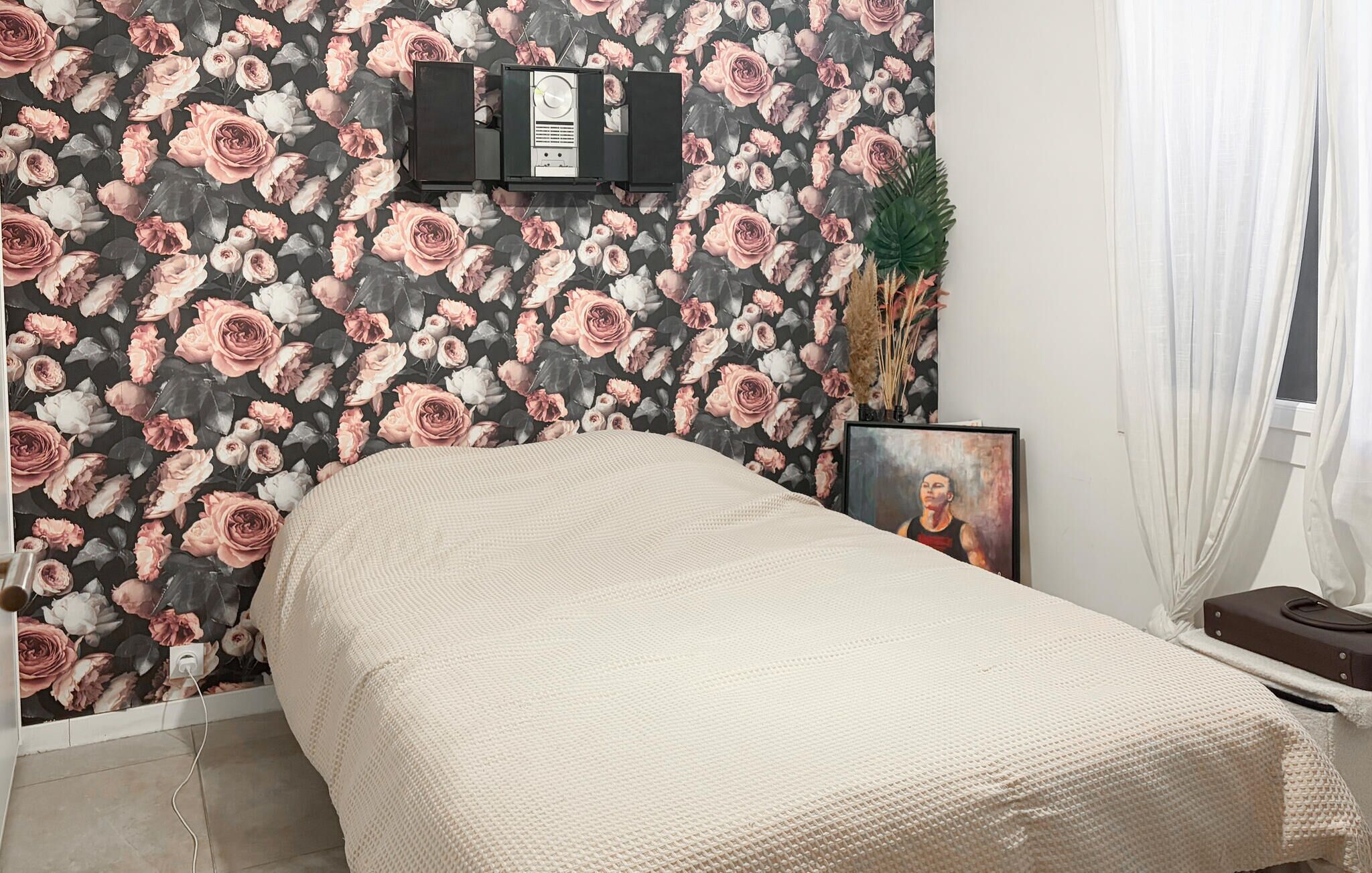 Une chambre à coucher avec un lit, un téléviseur fixé au mur, un tableau encadré et une plante.
