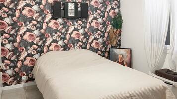 Une chambre à coucher avec un lit, un téléviseur fixé au mur, un tableau encadré et une plante.