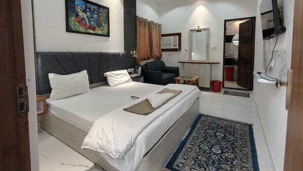 A hotel room with a bed, a desk, a chair, a TV, a mirror, and a painting on the wall.