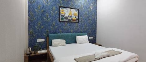 A bedroom with a bed, a nightstand, a framed picture, and a blue patterned wall.