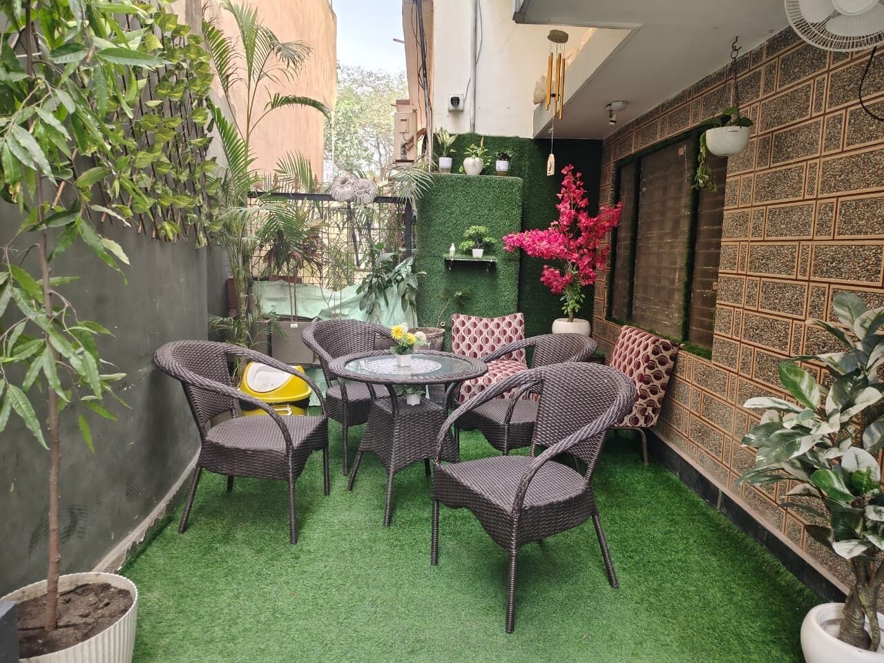 Un pequeño patio exterior con muebles de mimbre, una mesa redonda y plantas en macetas.