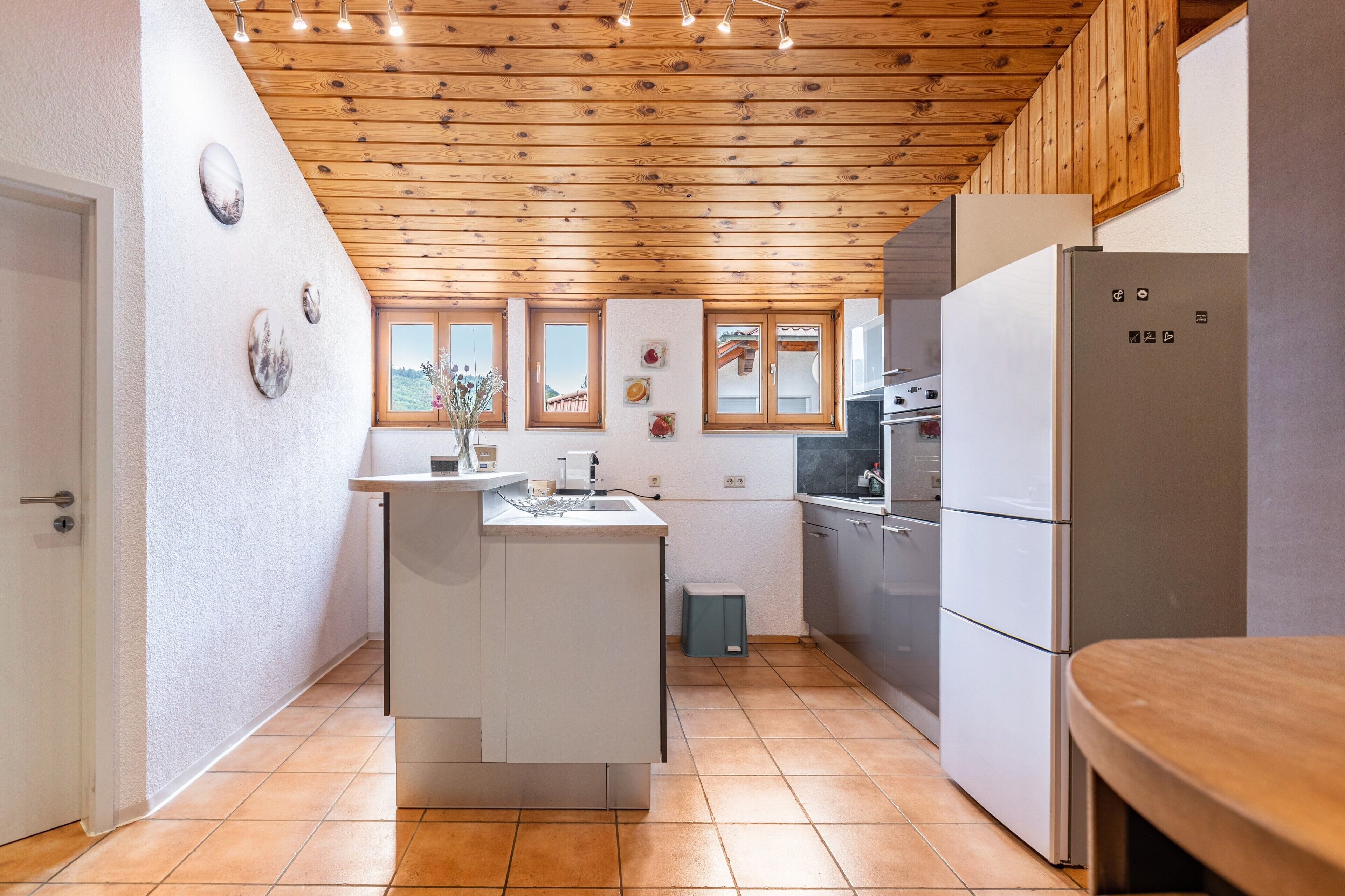 Eine kleine Küche mit Holzboden, weißen Schränken, einem eingebauten Ofen und einem Kühlschrank.
