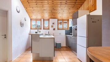 Eine kleine Küche mit Holzboden, weißen Schränken, einem eingebauten Ofen und einem Kühlschrank.