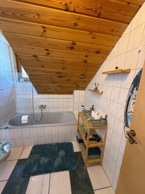 Ein Badezimmer mit Holzboden, einer Badewanne, einer Dusche, einem Ablagebereich für Pflegeprodukte und einem Handtuchhalter.