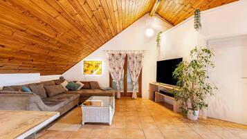 Ein gemütliches Wohnzimmer mit Holzbalkendecke, einer Couch, einem Couchtisch, einem Fernseher und einer Zimmerpflanze.