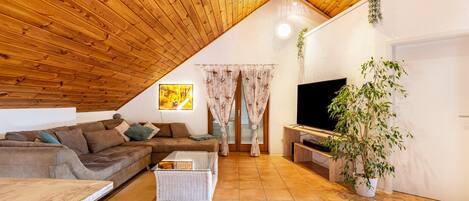 Un salon chaleureux avec un plafond en bois, un canapé, une table basse, un téléviseur et une plante en pot.