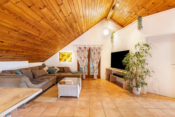 A cozy living room with a wooden ceiling, a sofa, a coffee table, a TV, and a potted plant.