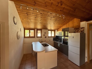 Une cuisine avec des poutres apparentes en bois au plafond, un îlot central, un réfrigérateur et un four à micro-ondes.