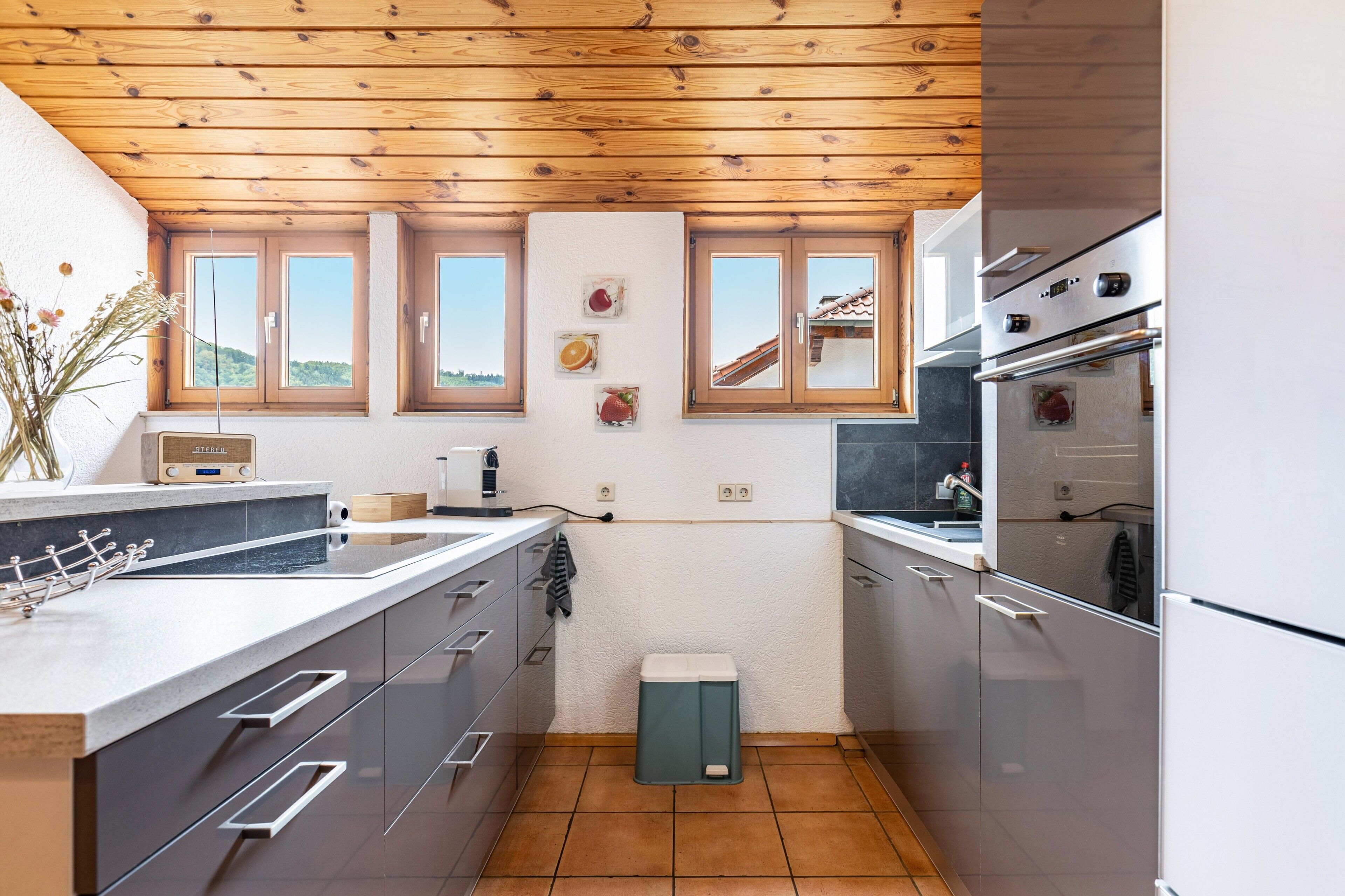 Eine moderne Küche mit Holzbalkendecke, einer großen Kochinsel und Blick auf die Landschaft durch die Fenster.