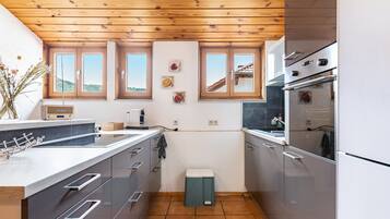 Eine moderne Küche mit Holzbalkendecke, einer großen Kochinsel und Blick auf die Landschaft durch die Fenster.