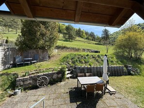 Une terrasse avec une table et des chaises, un mur en pierre et une pergola en bois.
