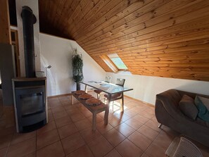 Une pièce chaleureuse avec un plafond en bois, un poêle à bois encastré, une table à manger avec des chaises et un canapé.