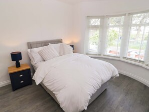 Ein Schlafzimmer mit einem Bett, einem Nachttisch, einer Lampe und einem Fenster mit Jalousien.