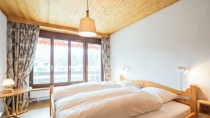 A bedroom with a wooden bed, a bedside lamp, a window with curtains, and a ceiling light.