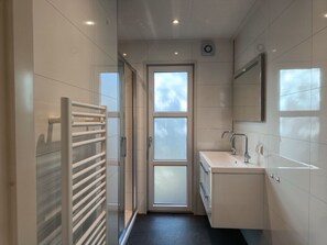 Een smalle badkamer met een glazen deur, een handdoekrek, een wastafel en een spiegel.