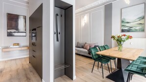 Una cocina moderna con horno integrado, un comedor con mesa de madera y sillas verdes, y un sofá gris al fondo.