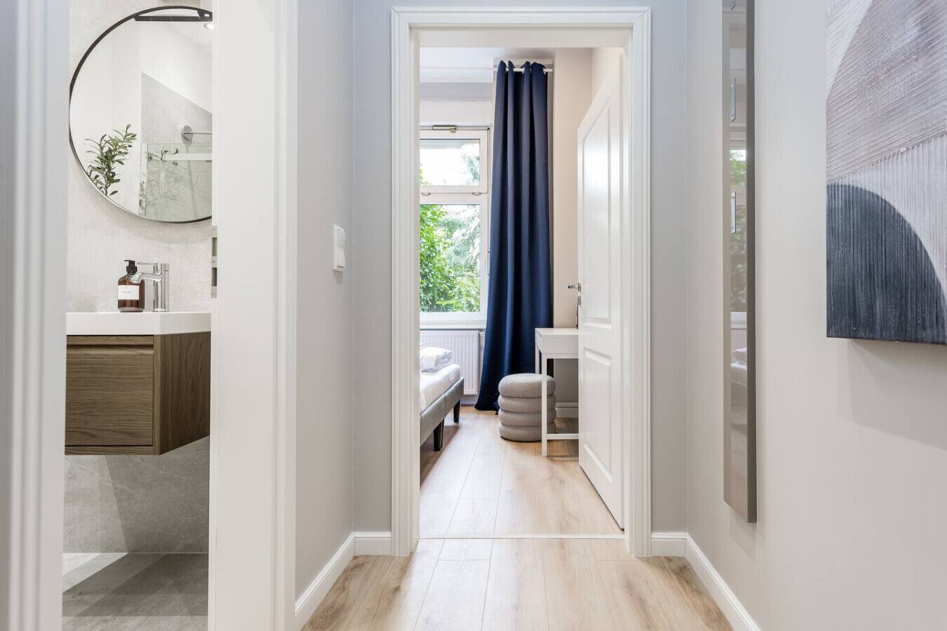 Ein Flur, der zu einem Schlafzimmer mit Fenster, Spiegel und einem Badezimmer mit Waschbecken und Spiegel führt.