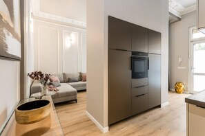 A modern kitchen with a built-in oven and microwave, a grey sofa, and a wooden coffee table. - Brand-new, designer 3-bedroom apartment (Berlin)