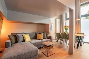 Ein modernes Wohnzimmer mit einem grauen Sofa, einem Glastisch und einem Essbereich mit einem Holztisch und Stühlen.