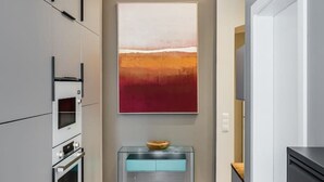 A modern kitchen with built-in appliances, a glass console table, and a large abstract painting on the wall. - Luxurious 3-Bedroom Designer Apartment (Berlin)