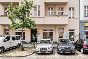 A street view with parked cars, a tree, and a building with a shop entrance. - Luxurious 3-Bedroom Designer Apartment (Berlin)