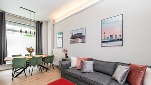 A modern living room with a grey sofa, green chairs, a red ottoman, and framed cityscape pictures on the wall. - Luxurious 3-Bedroom Designer Apartment (Berlin)