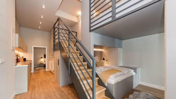 Un intérieur moderne avec un escalier menant à une chambre en mezzanine, un espace cuisine et une salle de bain ouverte.