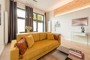 A modern living room with a sofa, a glass console table, and a painting on the wall. - Exclusive Designer Loft Near the Main Train Station (Berlin)