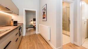 Une cuisine moderne avec un plan de travail en bois, un radiateur blanc et un couloir menant à une salle de bain dotée d’une douche en verre.
