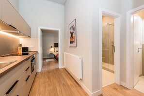 Eine moderne Küche mit einer Holzausziehtheke, einem weißen Heizkörper und einem Flur, der zu einem Badezimmer mit Glasdusche führt.