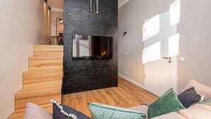 Un interior moderno con chimenea, escalera de madera y un sofá con cojines.