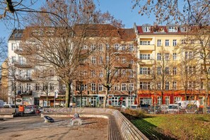 Reihenweise mehrstöckige Gebäude mit Balkonen, ein gepflasterter Bereich mit einer runden Bank und parkende Autos.