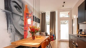 Un comedor moderno con una mesa de madera, sillas anaranjadas, un jarrón con flores y un cuadro abstracto grande en la pared.