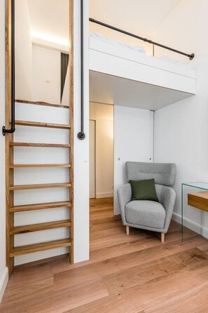 Ein modernes Interieur mit einer Holzleiter, einem grauen Sessel und einem Glastisch.