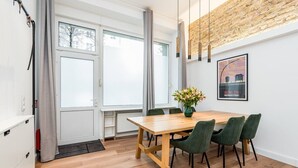 Ett modernt matområde med ett träbord, gröna stolar, en vas med blommor och en inramad tavla på väggen.