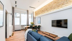 Ett modernt vardagsrum med en soffa, ett matbord med stolar, en TV som är monterad på väggen och en accentvägg i tegel.