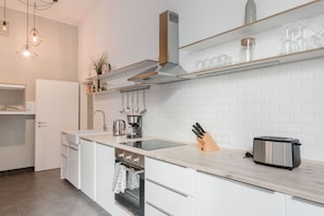 A modern kitchen with white cabinetry, a built-in oven, a stainless steel toaster, and hanging utensils. - Stylish Apartment in the Heart of Berlin (Berlin)