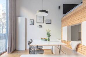 Ein moderner Essbereich mit einem weißen Tisch, grauen Stühlen, einer hängenden Leuchte und gerahmten Kunstwerken an der Wand.