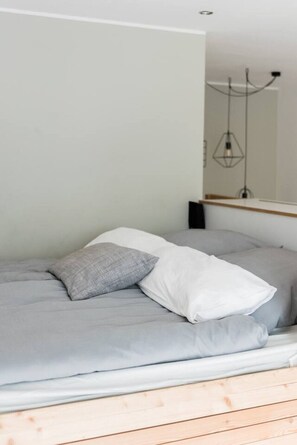 A bed with grey bedding and a pillow, a wooden headboard, and a hanging light fixture. - Stylish Apartment in the Heart of Berlin (Berlin)