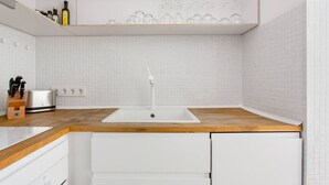 Cuina moderna amb rentatge blanc, taulell de fusta i armaris blancs.
