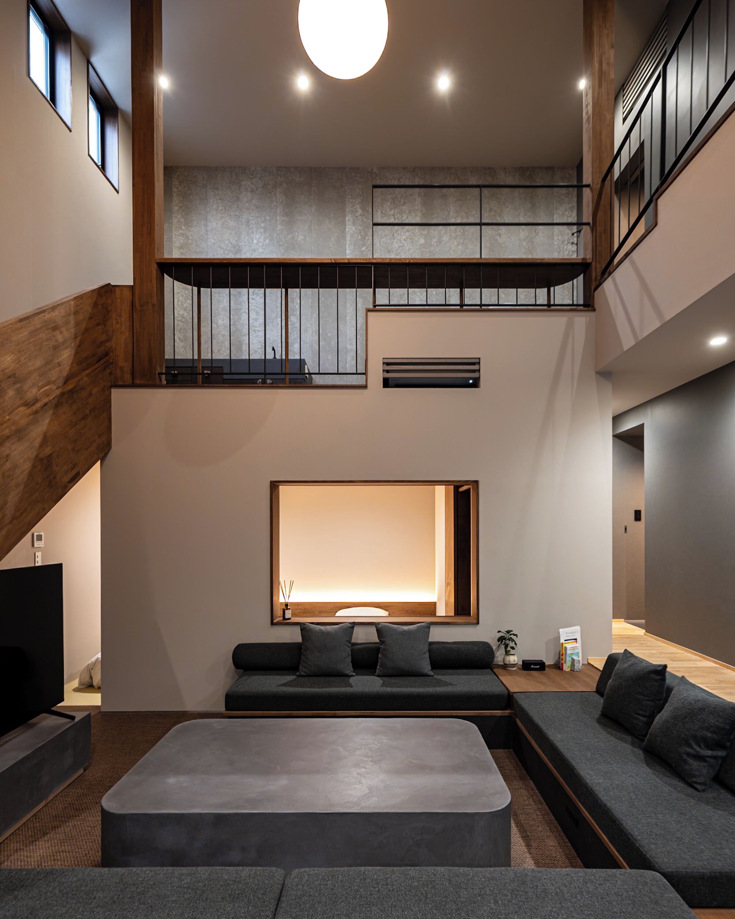 A modern interior with a large seating area, a staircase, and a high ceiling with recessed lighting.